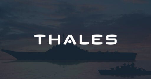 Image d'un transporteur militaire sur l'océan au coucher du soleil avec superposition du logo Thales.