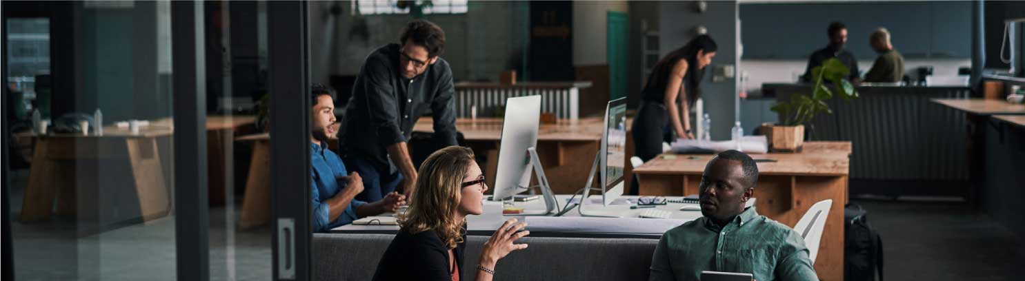 Imagen de personas en un entorno de trabajo de espacio abierto con computadoras y escritorios.