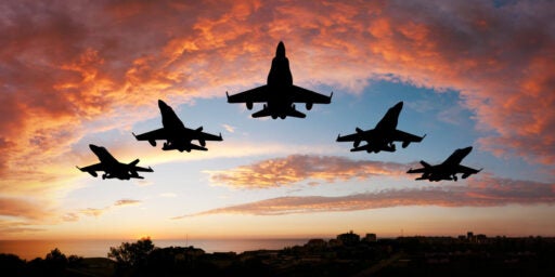 Image of five fighter jets flying above at sunrise.