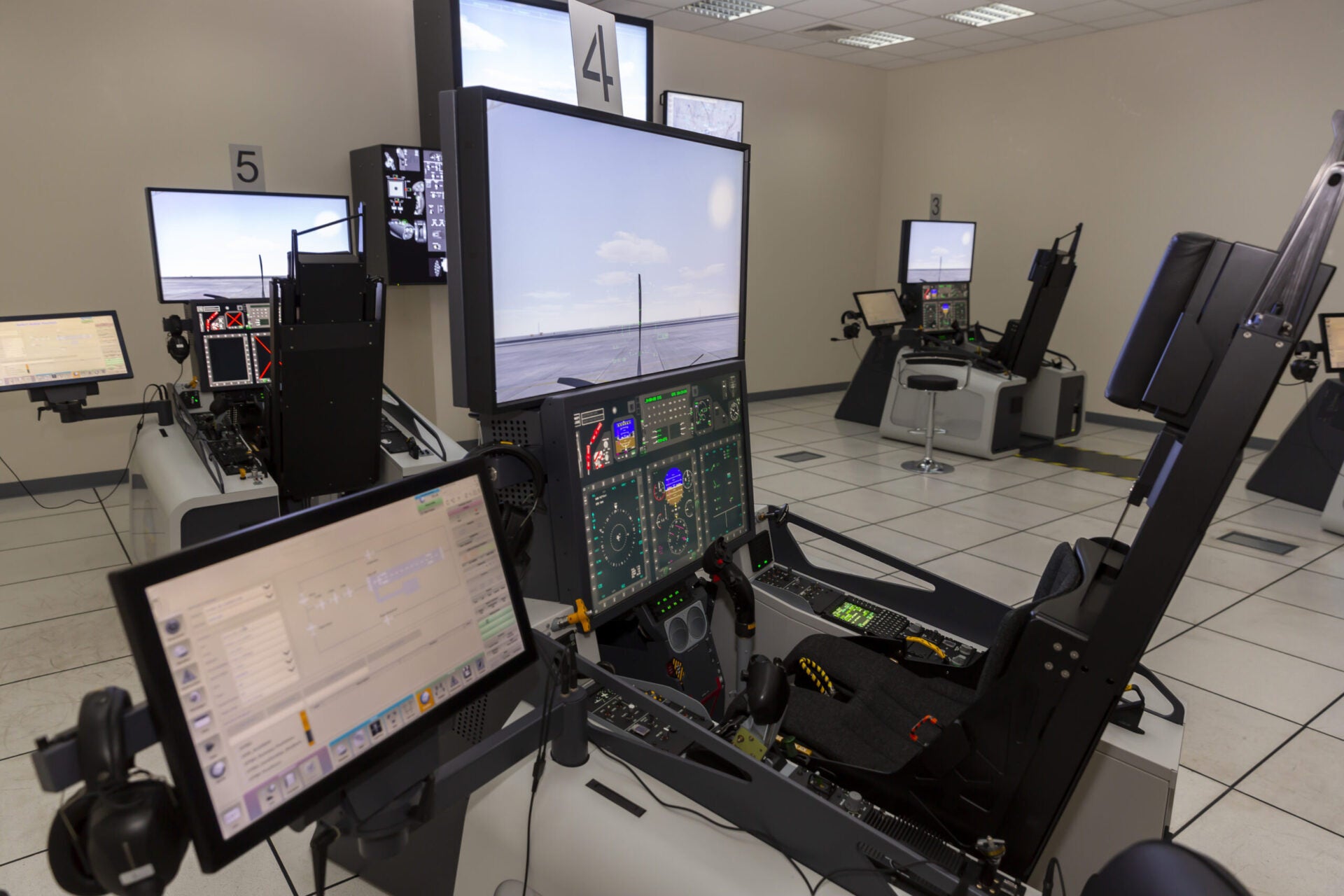 Image d'une salle de formation sur simulateur d'avion de chasse avec plusieurs écrans et commandes pour pratiquer la simulation d'environnement de test