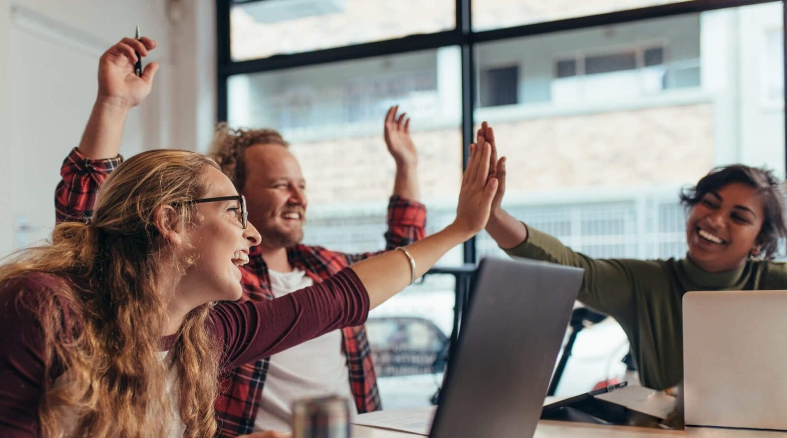 Image of group of colleagues sitting at table and giving each other high fives