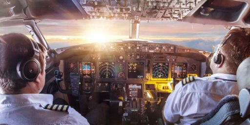 Bild eines großen Flugzeugcockpits, das in den Wolken fliegt und die Sonne ins Fenster strahlt.