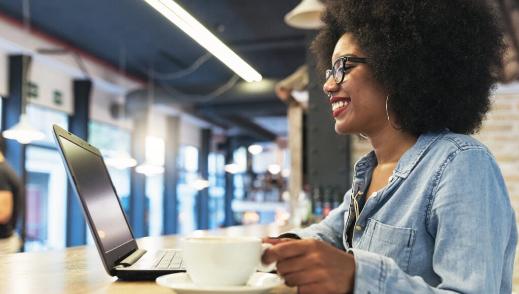 Mujer negra sonriendo mientras realiza pruebas API en su computadora portátil.