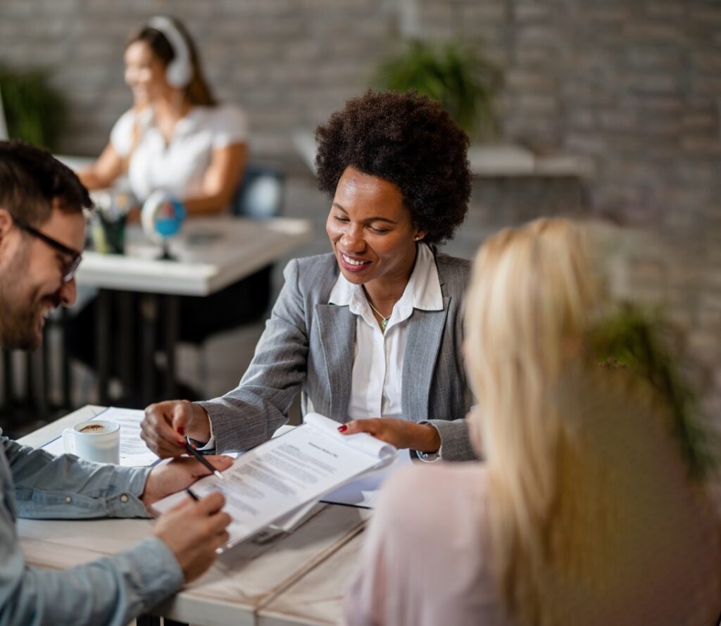 Image montrant une banquière professionnelle assise à un bureau avec des clients signant des documents.